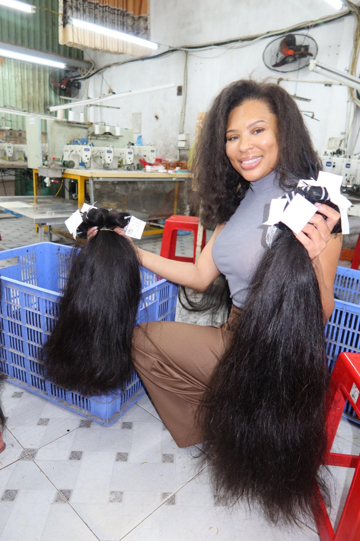 Erin in a hair factory holding two long bundles of hair